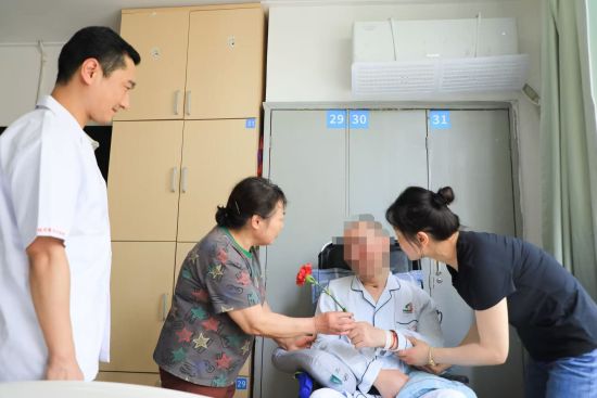 图为汤先生在妻子的帮助下为母亲献上一支康乃馨。西南医院江北院区供图 图为汤先生在妻子的帮助下为母亲献上一支康乃馨。西南医院江北院区供图